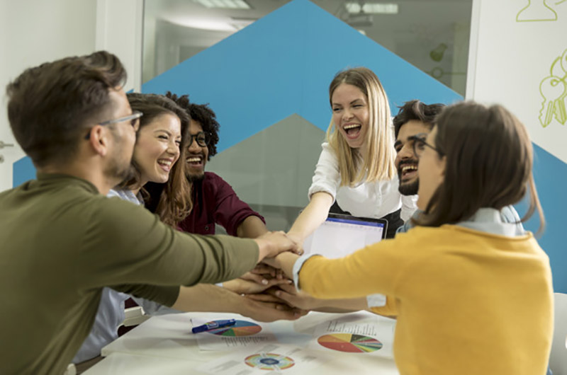 Team people stacking hands together over table engaged in teambu